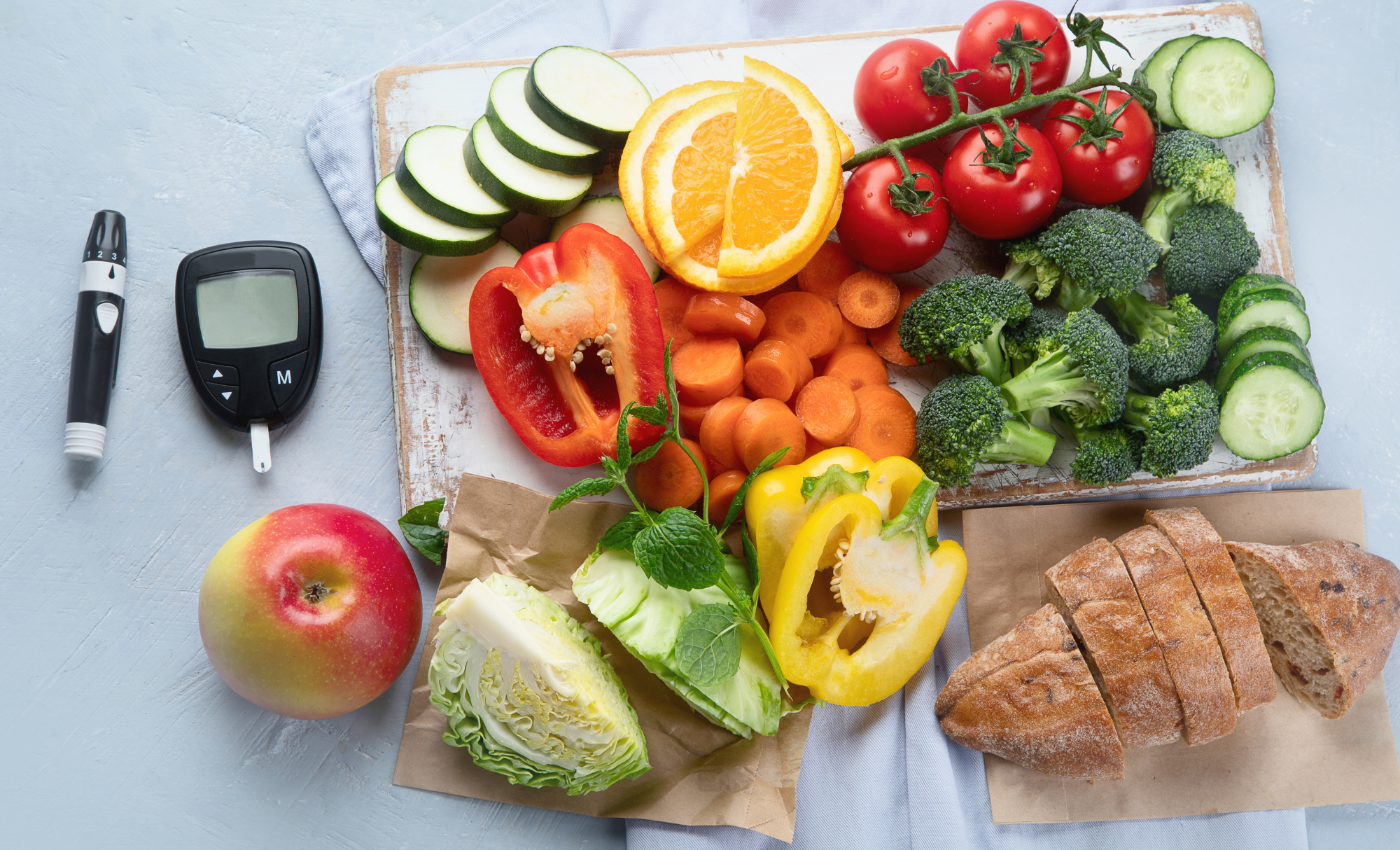 A board with assorted fruits, vegetables and bread. Beside it is a blood sugar reader.